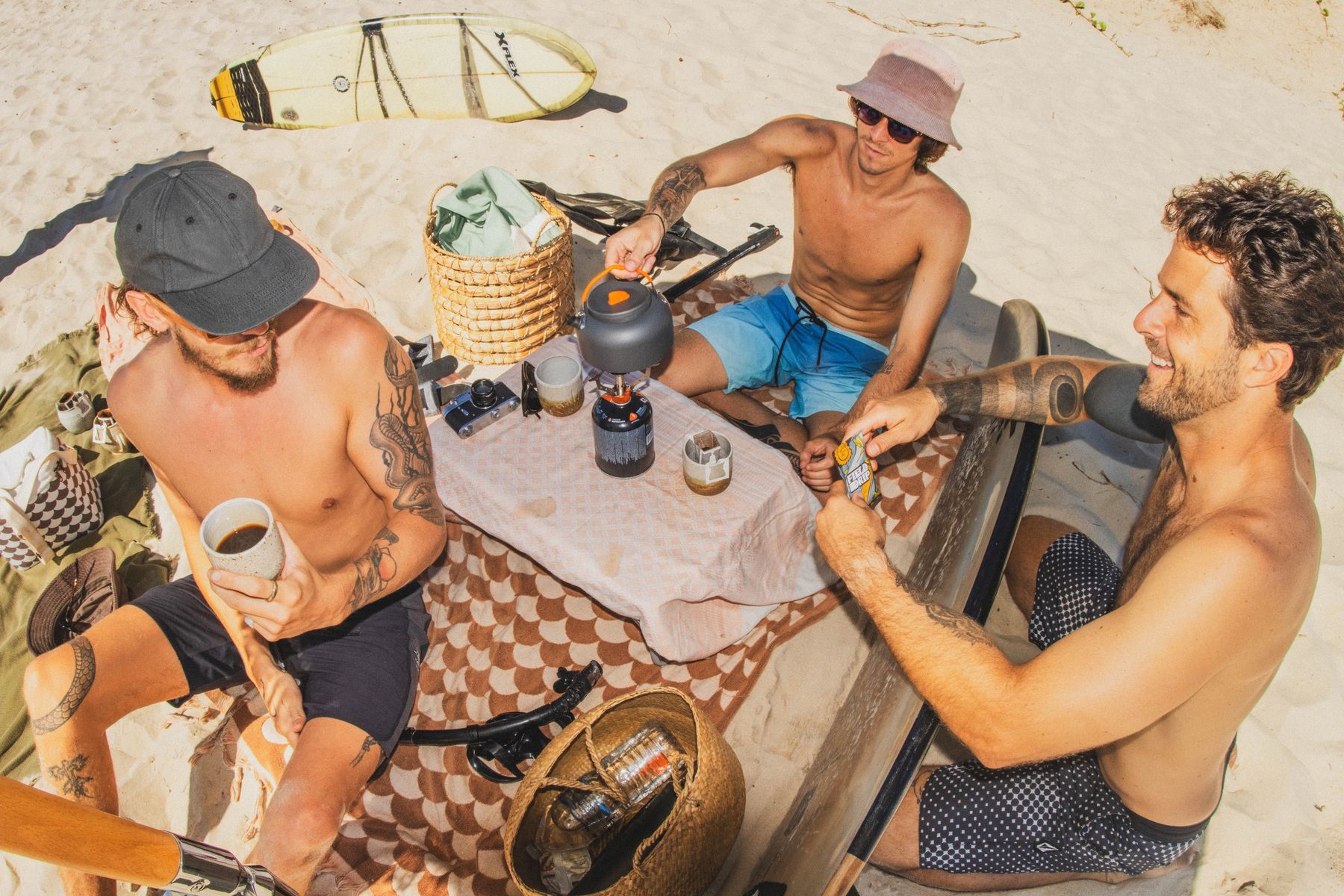 Friends brewing Field Drip coffee on the beach after a surf