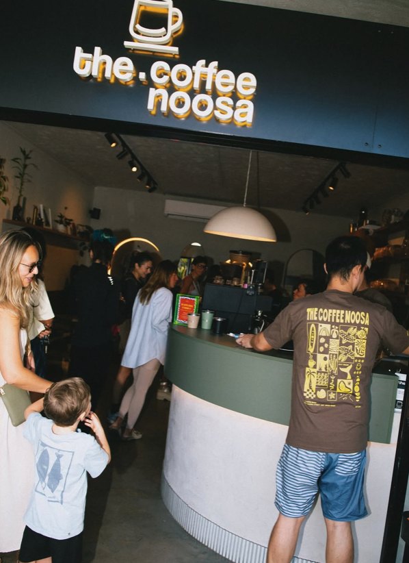 Customers in The Coffee Noosa merch at the busy counter under the new sign