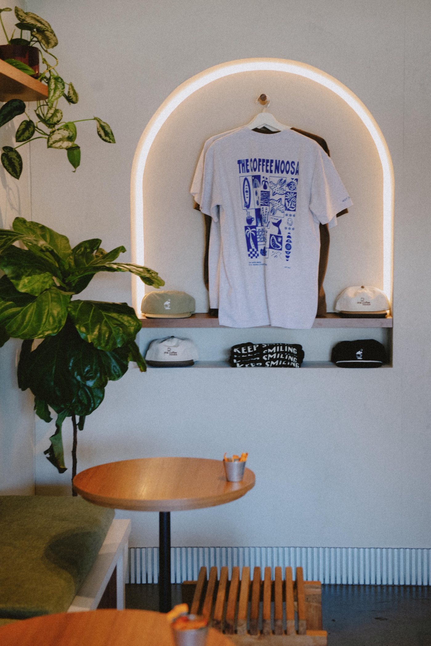 The Coffee Noosa t-shirt and caps on display in a lit arch inside the café